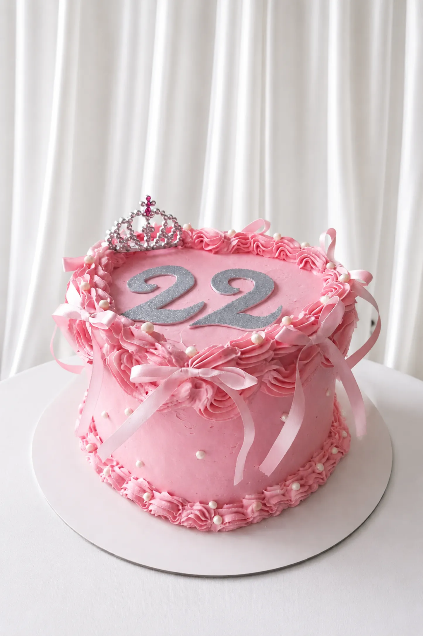 Bolo rosa de aniversário de 22 anos, com tiara, laços e pérolas
